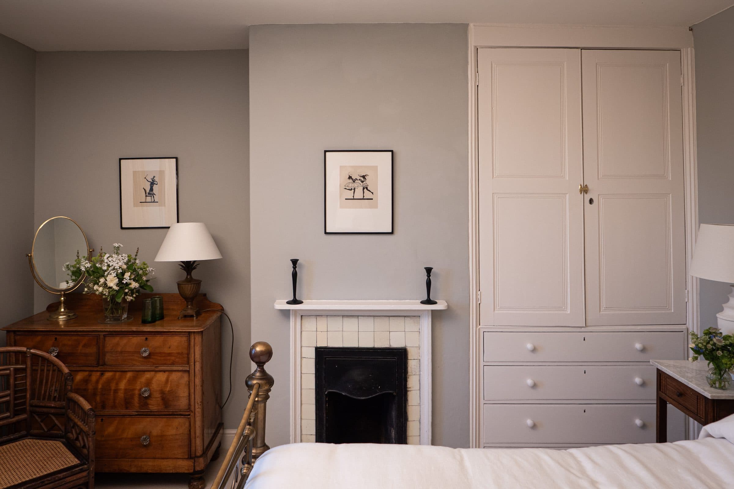 A bedroom with a painted linen press, marble fireplace, chest of drawers and a mirror above.