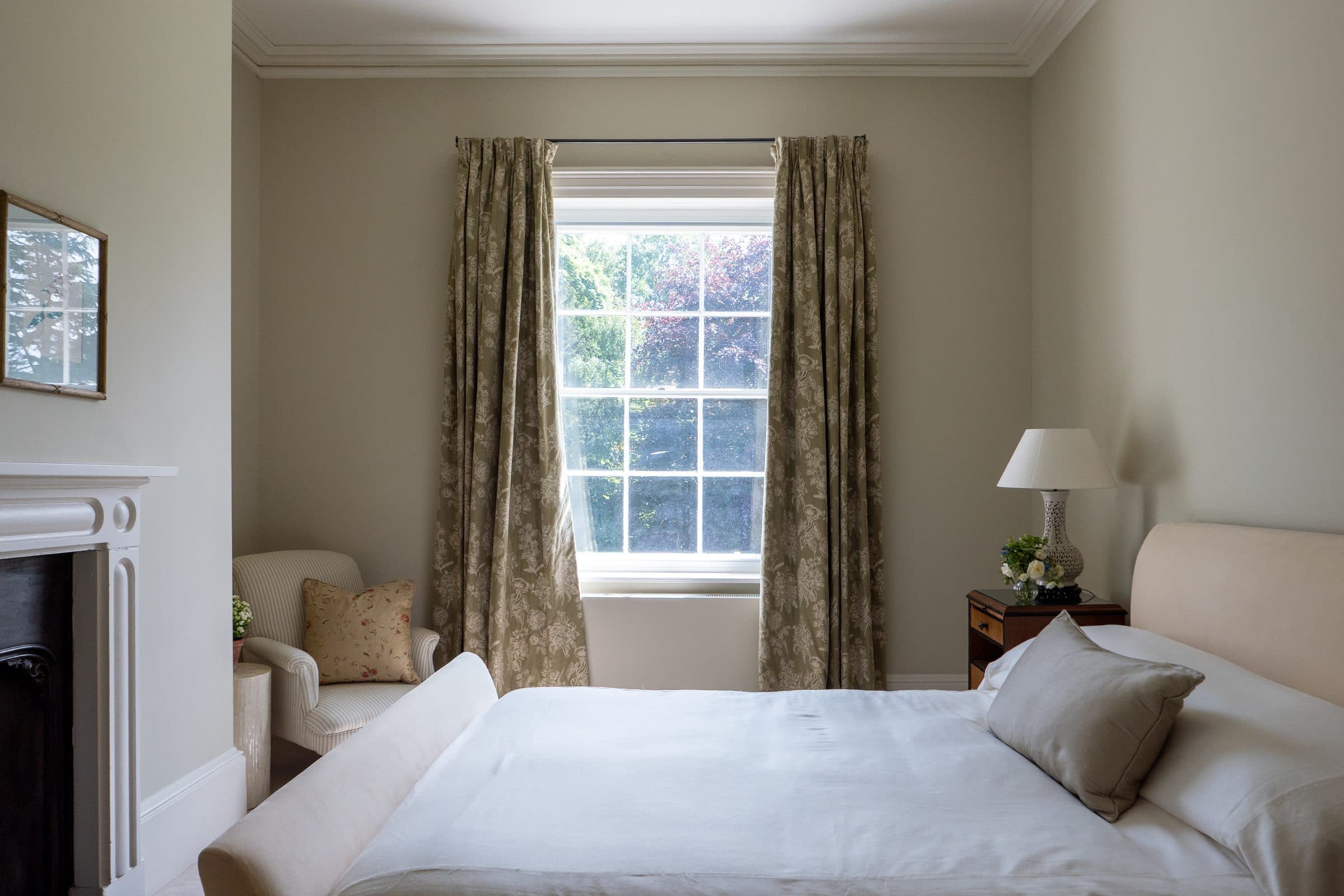 A double bedroom with the bed between a sash window and the fireplace, curtains drawn back to the garden.