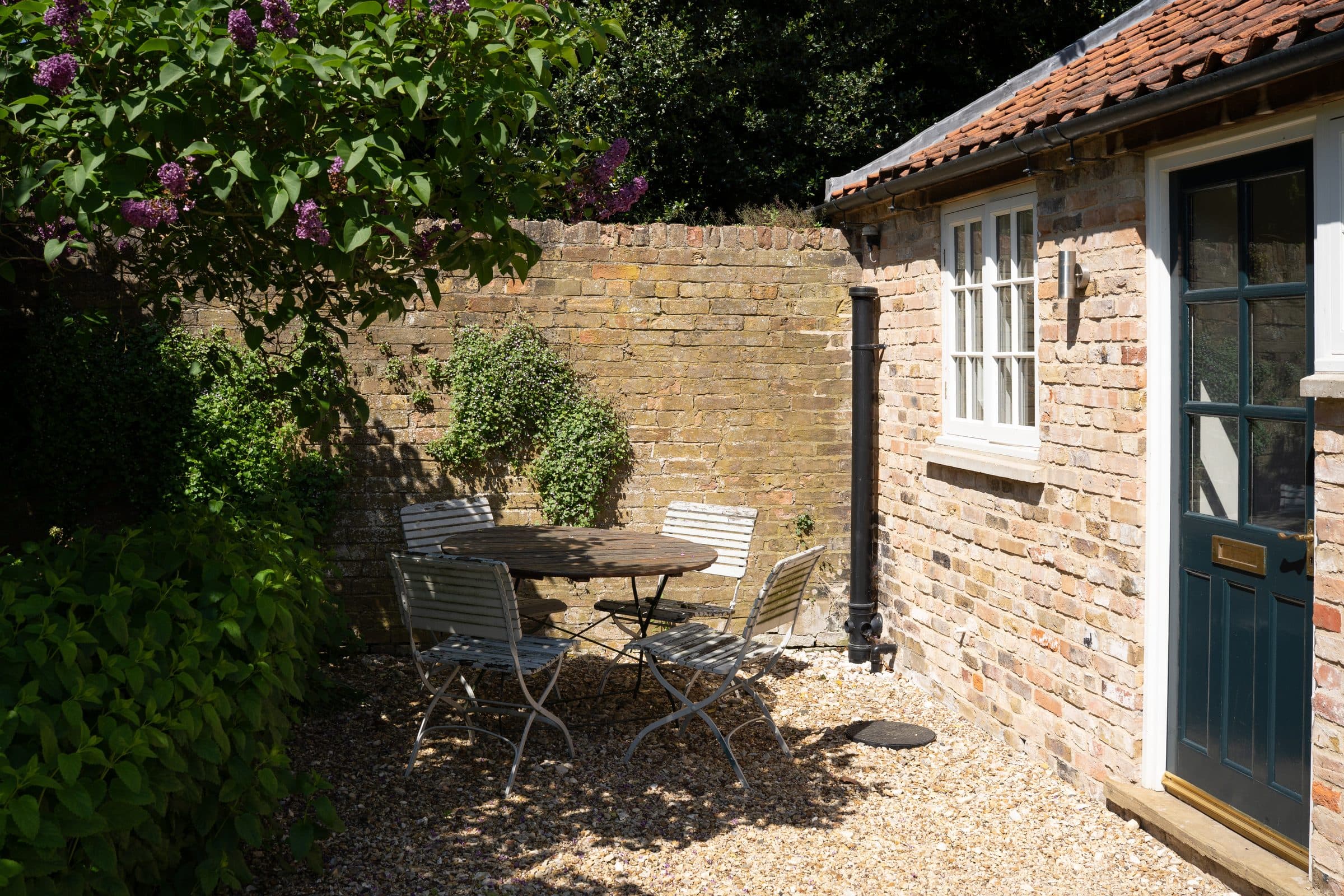 The Cottage door and window across the gravel courtyard, with a bistro table set beneath the wall.