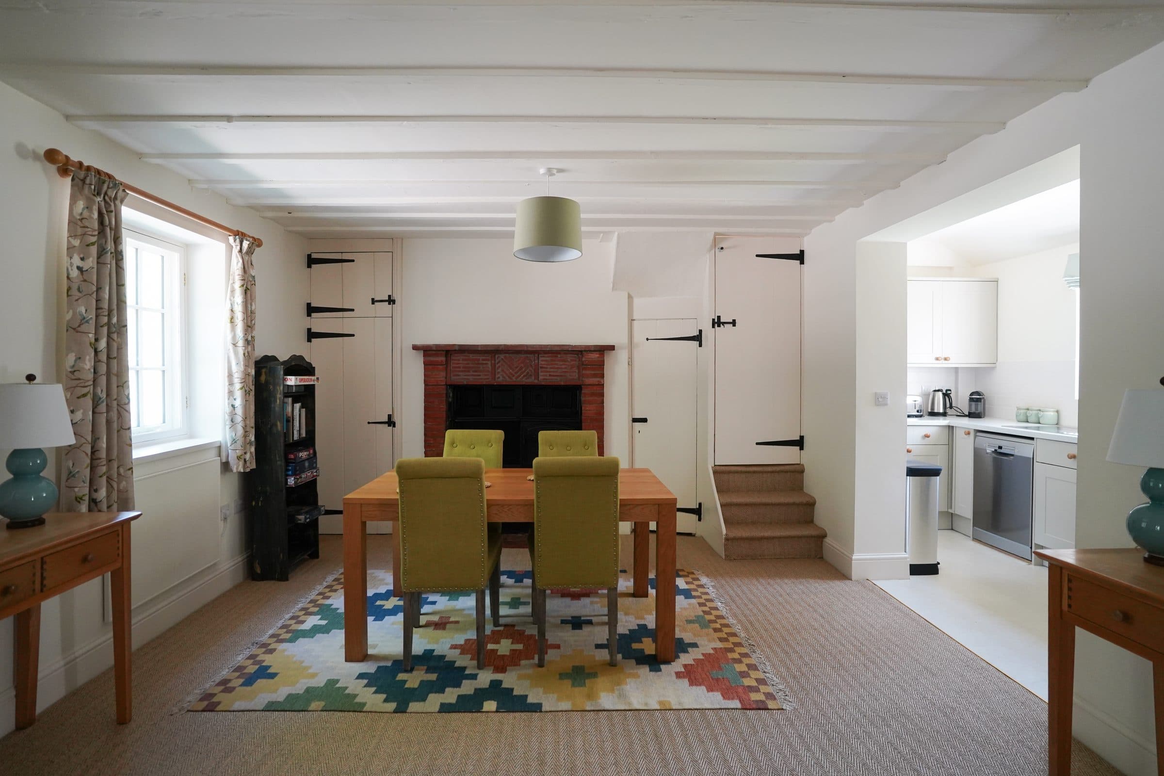The Cottage dining table beneath the beamed ceiling, with the kitchen through the doorway beyond.