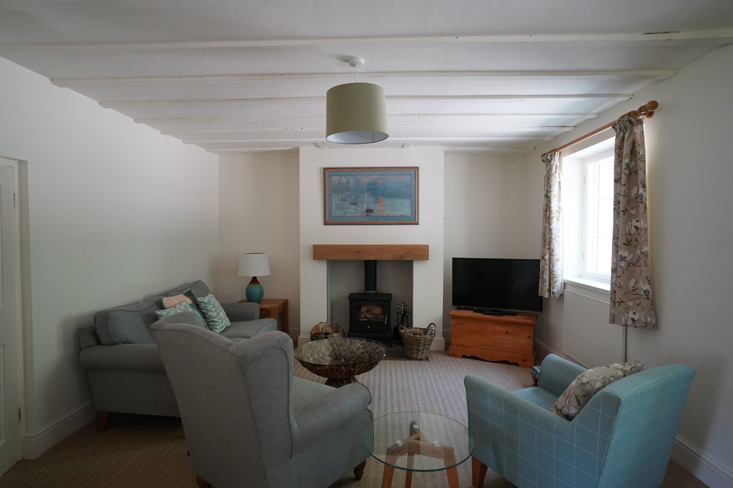 The Cottage living room under its boarded ceiling, with armchairs drawn up to the wood burner.