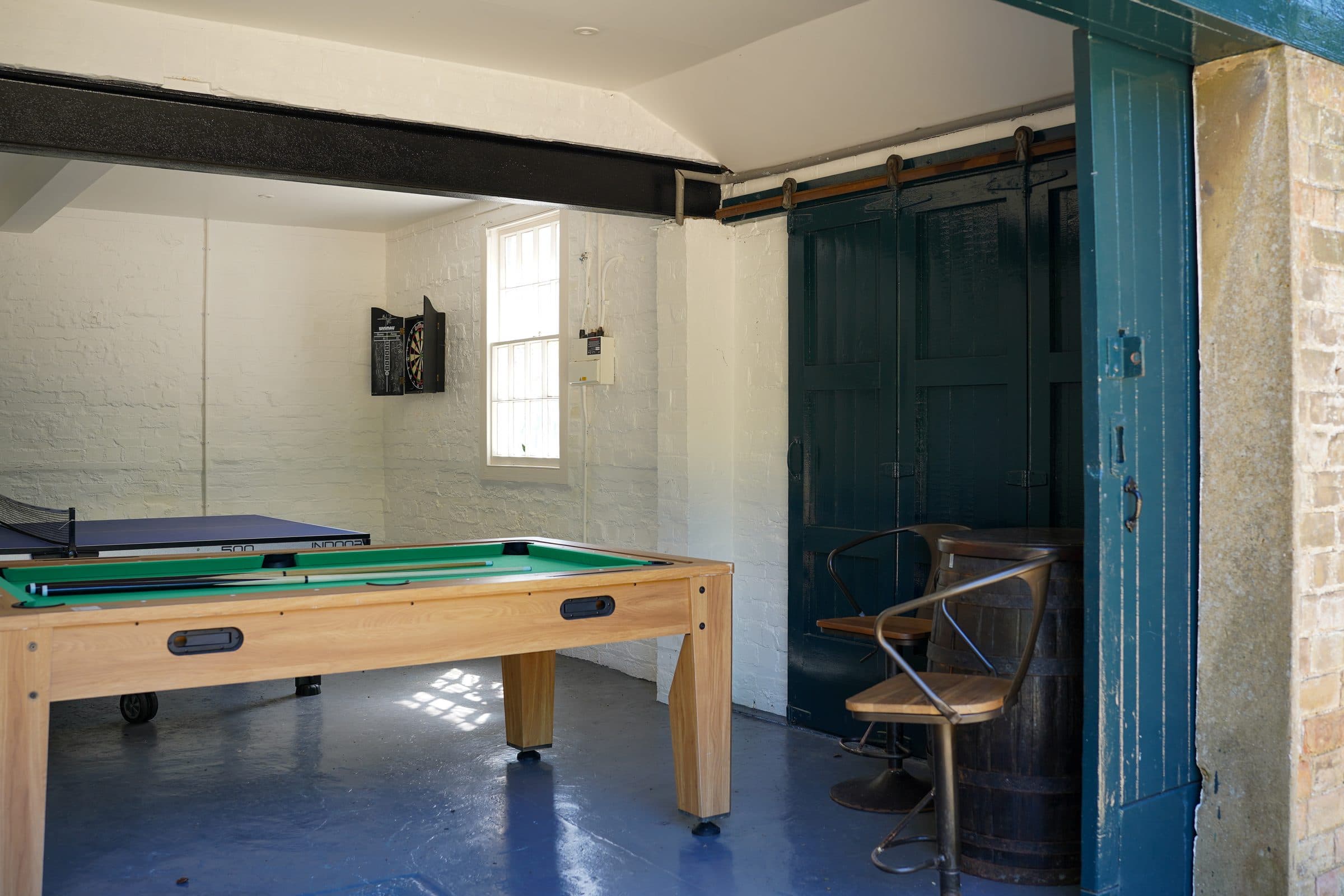 The games room in the outbuilding: a pool table under whitewashed walls, with the tall blue-green doors thrown open.