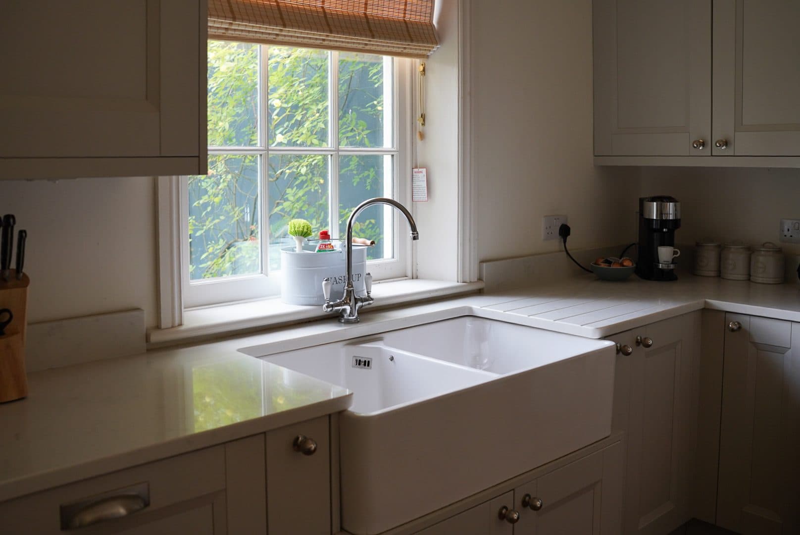 The kitchen with its butler sink under the window, cream cabinets and a view onto the garden.